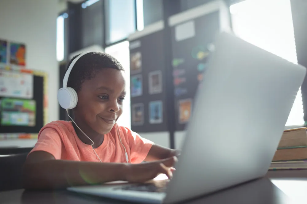 Image of a young black biy smiling while using a laptop